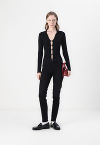 Svart langermet bodysuit med dyp V-hals og knappedetaljer, kombinert med høyt midje svarte jeans og glansede svarte loafers. Liten rød håndveske.