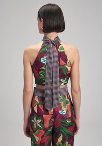 Crop top med blommönster i rik bordeaux, grönt och krämigt. Har en halterneck och en knytning i ryggen med rutiga accenter.