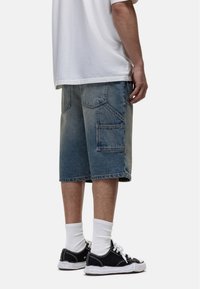 Niebieskie szorty cargo z denimu, z wieloma kieszeniami, długości do kolan i z wyblakłym wyglądem. W zestawie z czarnymi sneakersami i białymi skarpetkami typu crew.