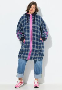 Cappotto in fleece a quadri navy e azzurro chiaro con zip e dettagli rosa. Presenta un cappuccio, una vestibilità ampia e tasche laterali. Abbinato a pantaloni in denim a vita corta.