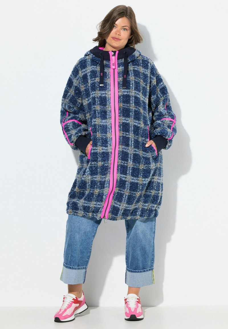 Cappotto in fleece a quadri navy e azzurro chiaro con zip e dettagli rosa. Presenta un cappuccio, una vestibilità ampia e tasche laterali. Abbinato a pantaloni in denim a vita corta.