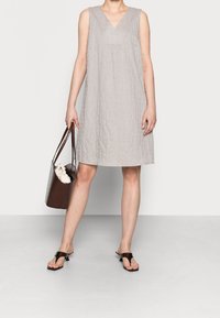 Jasnoszara, lniana sukienka bez rękawów, projekt z dekoltem w serek, lekko teksturowany materiał. Brązowa, pleciona torba na ramię z akcentowanymi uchwytami i białym przedmiotem wewnątrz.