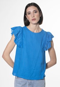 Top in lino blu con maniche in pizzo arricciato, scollo rotondo e vestibilità comoda. Design semplice con una texture sottile e un colore vivace.