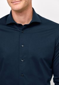 Camicia button-up blu navy in tessuto morbido, con colletto all'inglese e bottoni neri, mostrata in una vista ravvicinata.