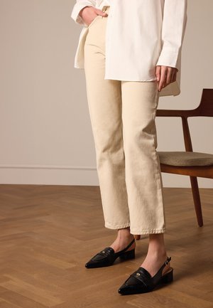 Pantalons crème, à jambe droite, associés à des escarpins noirs à bout pointu et dos ouvert, dotés d'un petit talon bloc et d'un détail doré.