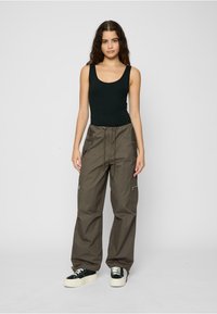 Black sleeveless top and loose-fit olive cargo pants with a drawstring waist, zip pockets, and elastic cuffs. White and black sneakers.