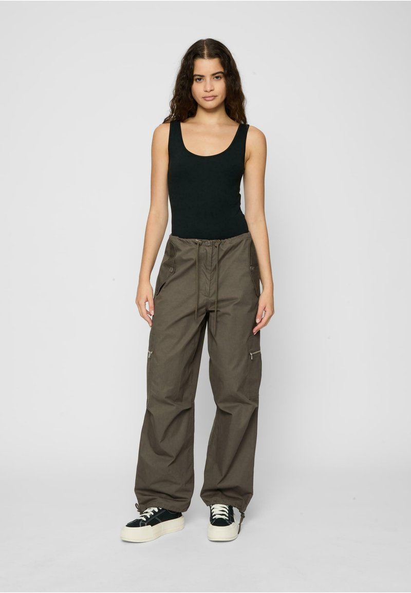 Black sleeveless top and loose-fit olive cargo pants with a drawstring waist, zip pockets, and elastic cuffs. White and black sneakers.