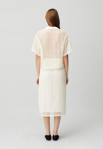Ensemble léger en deux pièces de couleur crème avec un motif à carreaux ; haut à manches courtes et jupe mi-longue. Texture lisse, accompagné de chaussures noires.