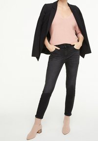 Czarne skinny jeans zestawione z różową bluzką o prążkowanej strukturze oraz oversize'ową czarną marynarką; różowe botki za kostkę na szerokim obcasie dopełniają stylizację.