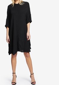 Svart knapp-up klänning med korta ärmar, har en avslappnad passform, flödande tyg, knälång fåll och minimalistisk design.