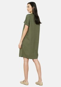 Vestido de lino verde oliva con mangas cortas, costuras laterales y un corte holgado, combinado con zapatos abiertos beige.