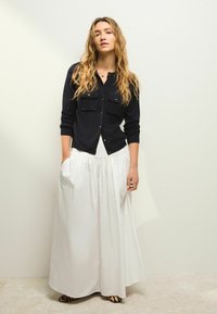 Navy button-up shirt with chest pockets, paired with a white, flowy pleated maxi skirt. Black and beige leopard print shoes.