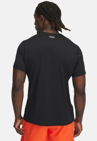 Zwarte sportshirt met korte mouwen en een ronde hals. Heeft een klein merkje in het wit op de bovenrug. Glad stof, getailleerd ontwerp.