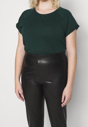 Mørkegrøn kortærmet top med raglanærmer, kombineret med højtaljede sorte bukser i imiteret læder, glat tekstur og tætsiddende design.