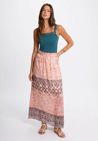 Top corto turchese con spalline a onde, abbinato a una lunga gonna rosa con motivo floreale caratterizzata da bordi intricati e una vita arricciata.