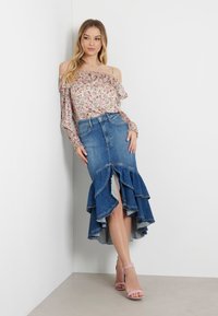 Blomstret off-shoulder bluse med flæserærmer, parret med en højtaljet denimnederdel med tierede flæser og en forretningsslids. Lyserøde hæle.