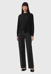 Maglione nero a maglia testurizzata con design asimmetrico, abbinato a jeans neri a gamba larga e scarpe nere con dettagli dorati.