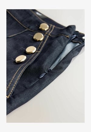 Dark denim trousers featuring gold buttons, contrasting stitching, and a side zip closure. The fabric has a smooth texture.