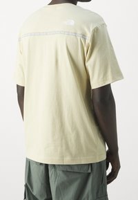 Krémové bavlněné tričko s krátkým rukávem, na kterém je velké logo a text přes záda, s kulatým výstřihem a volným střihem.