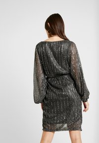 Schwarzes, mit Pailletten besetztes Kleid mit lockerem Schnitt, langen, durchsichtigen Ärmeln und gerafft Taille. Vertikale Streifen erzeugen eine strukturierte Optik.