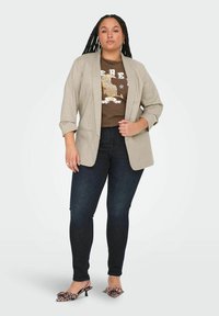 Heledbeez žaket rullitud varrukatega pruunist graafilisest t-särgist, kombineeritud tumedate teksade ja leopardimustriga kontsakingadega.