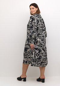 Robe à motif tourbillonnant noir et blanc avec des manches longues, un col et une longueur mi-mollet, associée à des sandales à talons bloc noires.