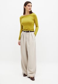 Maglietta a maniche lunghe di colore giallo senape con scollatura a barca abbinata a pantaloni larghi a vita alta di colore crema fissati da una cintura nera.