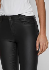 Pantalon noir en cuir synthétique avec coupe slim, poches avant et fermeture à boutons. Texture lisse avec un léger éclat.