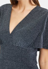 Třpytivé námořnicky modré šaty s hlubokým výstřihem do V, krátkými volánovými rukávy a texturovanou látkou. Příznivý střih zvýrazňuje pas.