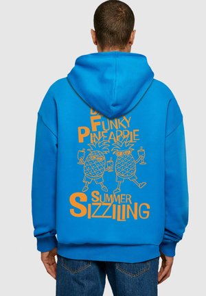 Kék kapucnis pulóver, amelyen egy vidám narancssárga grafika látható két napszemüveges ananásszal, italokkal, és a szöveg: "FUNKY PINEAPPLES SUMMER SIZZLIN."
