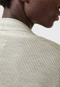 Maglietta a coste grigio chiaro che mostra un primo piano del colletto e del retro, con una finitura texture e sottili linee orizzontali.