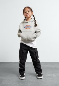 Grey hoodie with "Dickies" logo, front pocket, layered over a white shirt; black cargo pants, and black sneakers with white soles.