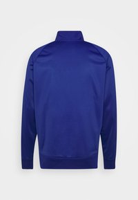 Giacca da track di colore blu navy con colletto alto, maniche lunghe e polsini a coste. Tessuto liscio con un design semplice, senza motivi o dettagli notevoli.