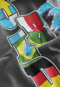 Gros plan d'un imprimé textile montrant des lettres stylisées avec les drapeaux italien, brésilien et allemand sur un fond sombre.