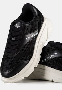 Baskets noires avec des matériaux en mesh et en cuir, dotées d'une épaisse semelle blanche, de lacets ronds et de la marque "CPH STUDIOS".