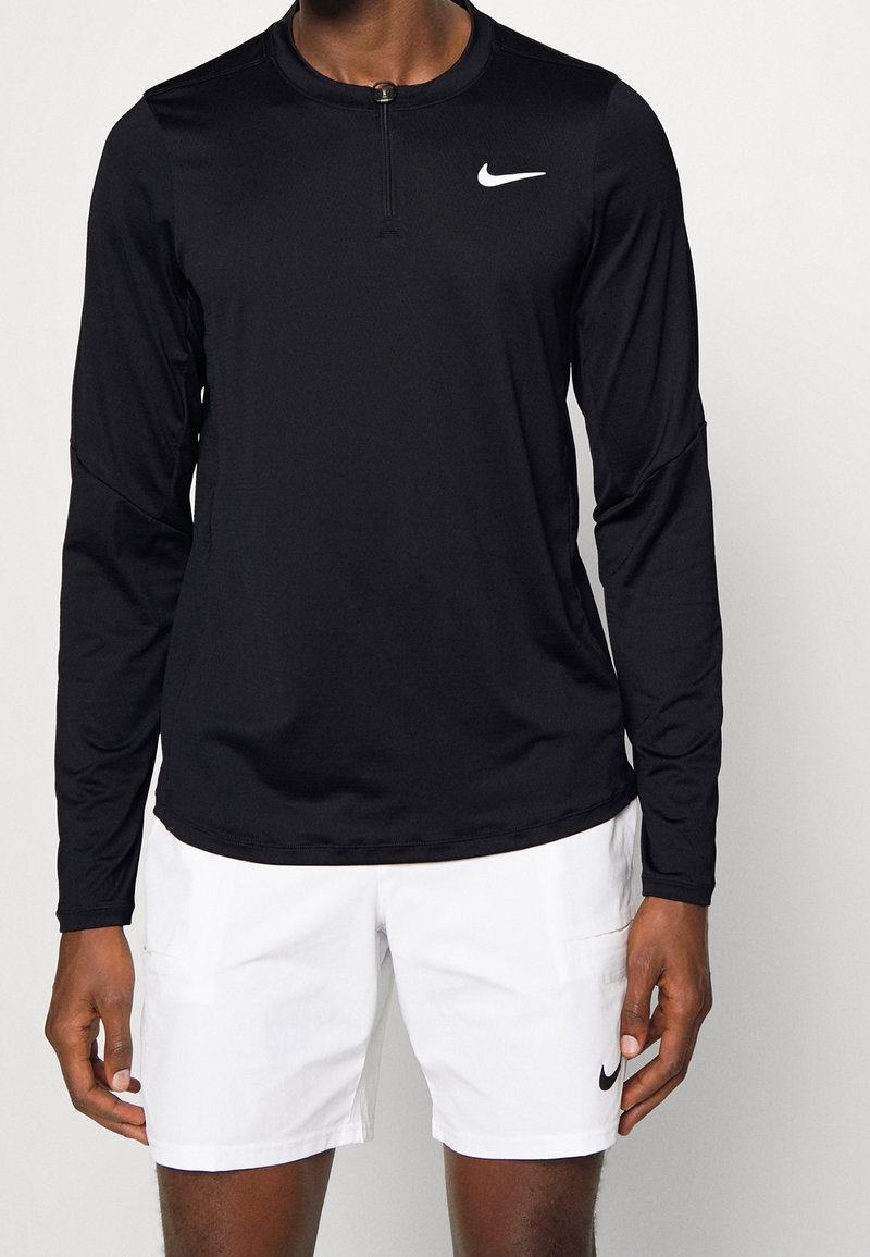 Musta pitkähihainen urheilu-paita, jossa on neljännesvetoketju kauluksessa ja valkoinen Nike-logo vasemmassa rinnassa. Sujuva, kevyt kangas.
