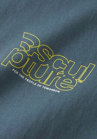 Zils audums ar lieliem dzelteniem burtiem, kuros rakstīts "skulptūra", un zem tā ir mazāka frāze "NĀKOTNES CILVĒKIEM". Tekstūrēta virsma.