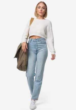 Hvid cropped sweater, lyseblå høj taljet jeans og hvide sneakers. Bærer en stor olivengrøn tote bag. Minimalistisk design.