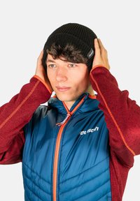 Black ribbed beanie worn by a person with brown hair, paired with a blue insulated jacket featuring red accents and a logo on the chest.