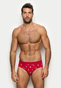 Røde bikini-trusser med et teddy bear-mønster, elastisk talje og en glat bomuldsstruktur. Modellen har en muskuløs bygning.