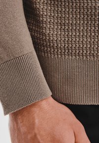 Brązowy sweter o teksturowej fakturze z prążkowanymi mankietami, z charakterystycznym wzorem w plaster miodu na korpusie i gładkim splotem na dole.