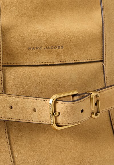 Sac en daim beige avec une ceinture assortie, doté d'une boucle dorée gravée de "Marc Jacobs" et "Marc Jacobs" embossés au-dessus du rabat.