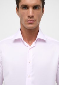 Lichtroze button-up shirt van gladde stof. Beschikt over een klassieke kraag en parelknopen aan de voorkant.