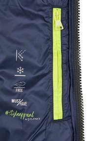 Interno di un piumino blu navy con una zip verde lime brillante, simboli di resistenza all'acqua e testo con scritto "GRATIS" e "DA AVERE ASSOLUTAMENTE".