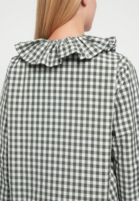 Zielono-biała koszula w kratę z teksturowanym marszczonym kołnierzem, prezentująca nadrukowany wzór i miękki materiał, widziana od tyłu.