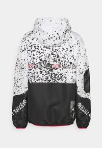 White and black hooded jacket with abstract speckled pattern, red accents on elastic cuffs, and decorative text across the upper back.