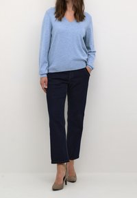 Light blue v-neck sweater in soft texture paired with dark blue straight-leg jeans. Beige high-heeled shoes complete the outfit.
