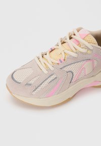 Beige Sportschuh aus Netz- und Wildledermaterialien. Mit rosa und grauen Akzenten, einer Gummisohle und einem runden Zehendesign.