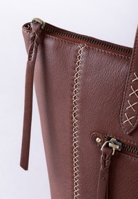 Brown leather tote bag featuring a textured surface, decorative stitching, a zip closure, and a braided strap detail.