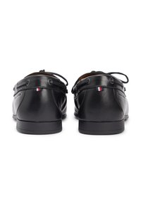 Μαύρα δερμάτινα παπούτσια σκαφών με στρογγυλεμένες φτέρνες, με κορδόνια και μια μικρή διακοσμητική σημαία τριχρώμου στην πλευρά. Λεπτή υφή.